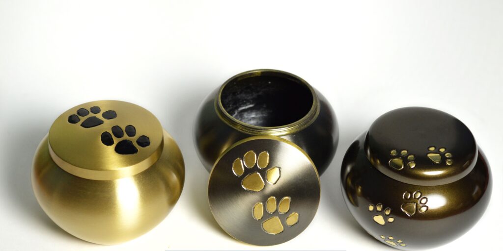 Three decorative pet cremation urns in gold and bronze finishes with engraved paw print designs, displayed on a white background.
